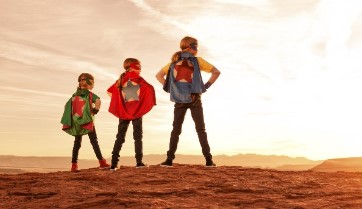 Three children wearing super hero costumes looking toward the horizon